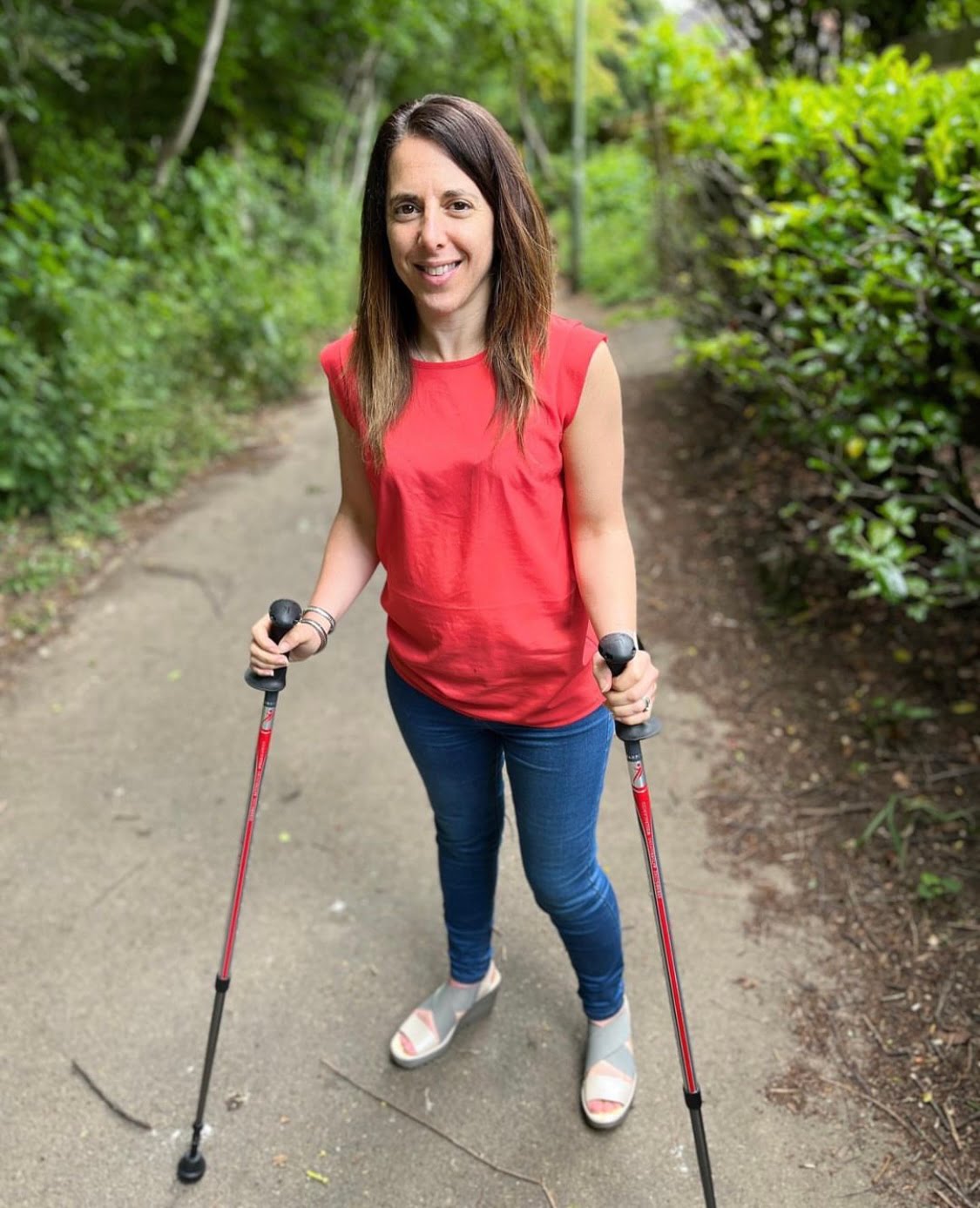 Photo of Georgina, Founder of Purpl, standing on a pathway with two walking poles in her hands. She has long dark hair and is wearing a red top and denim jeans.