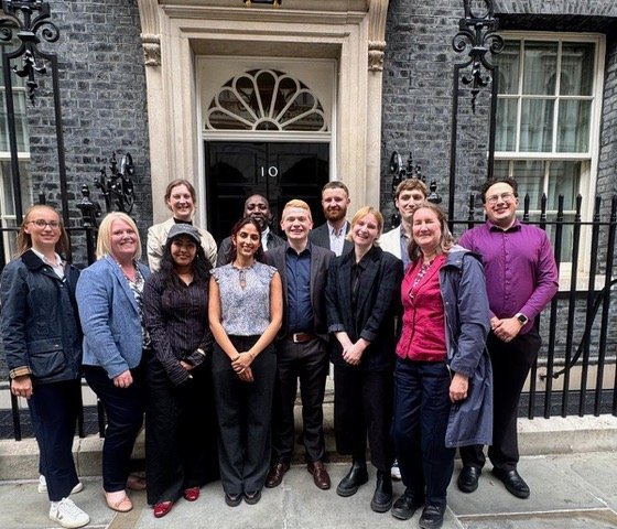 Group picture of the Generation Rent team posing together outside the black front door of 10 Downing Street in London.